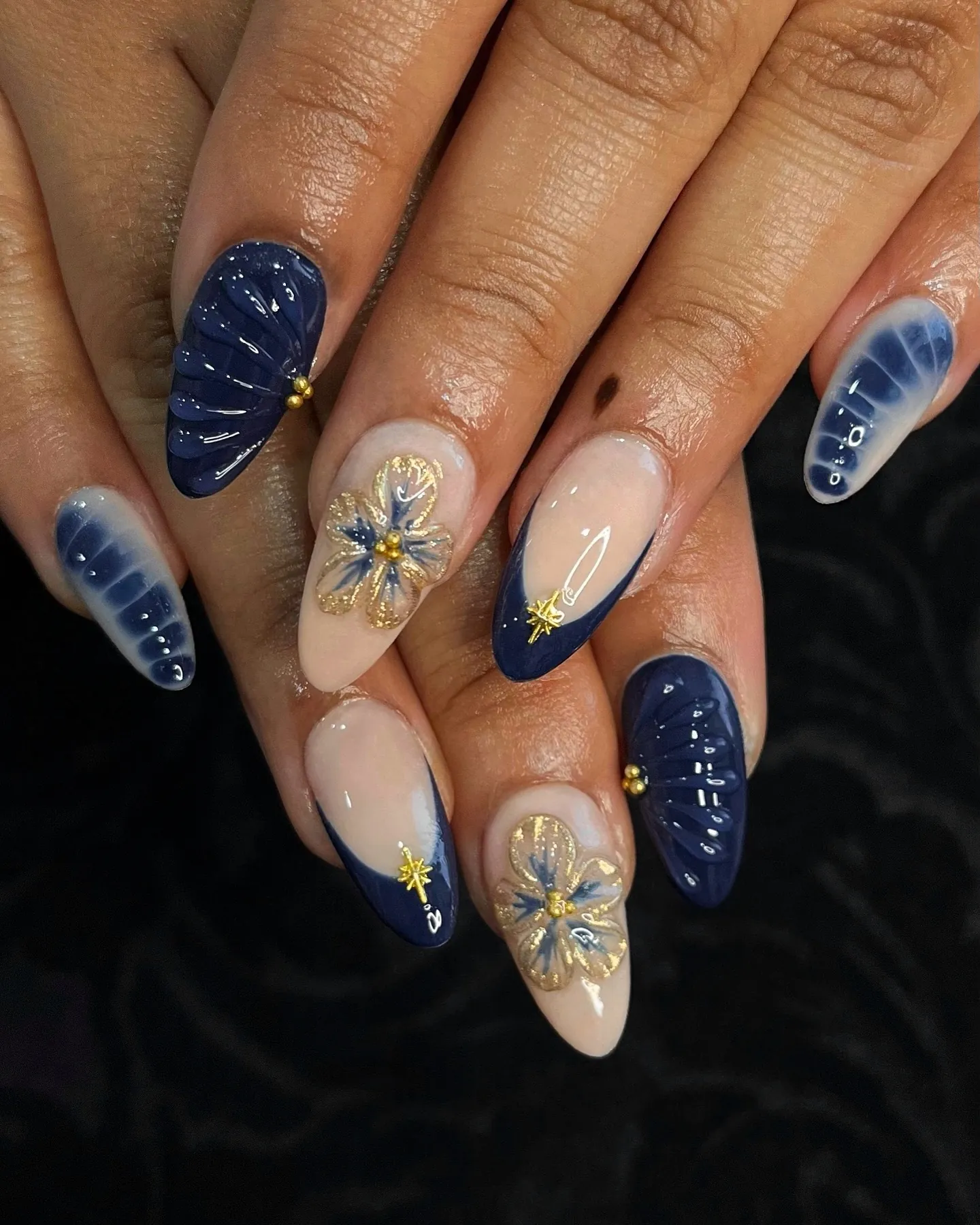 Navy and nude almond nails with gold outlined flowers, ridges and star accents