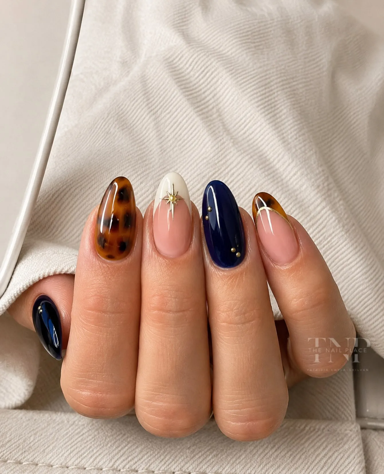 Almond nails mixing navy solids, nude gold star accents and a brown spotted pattern