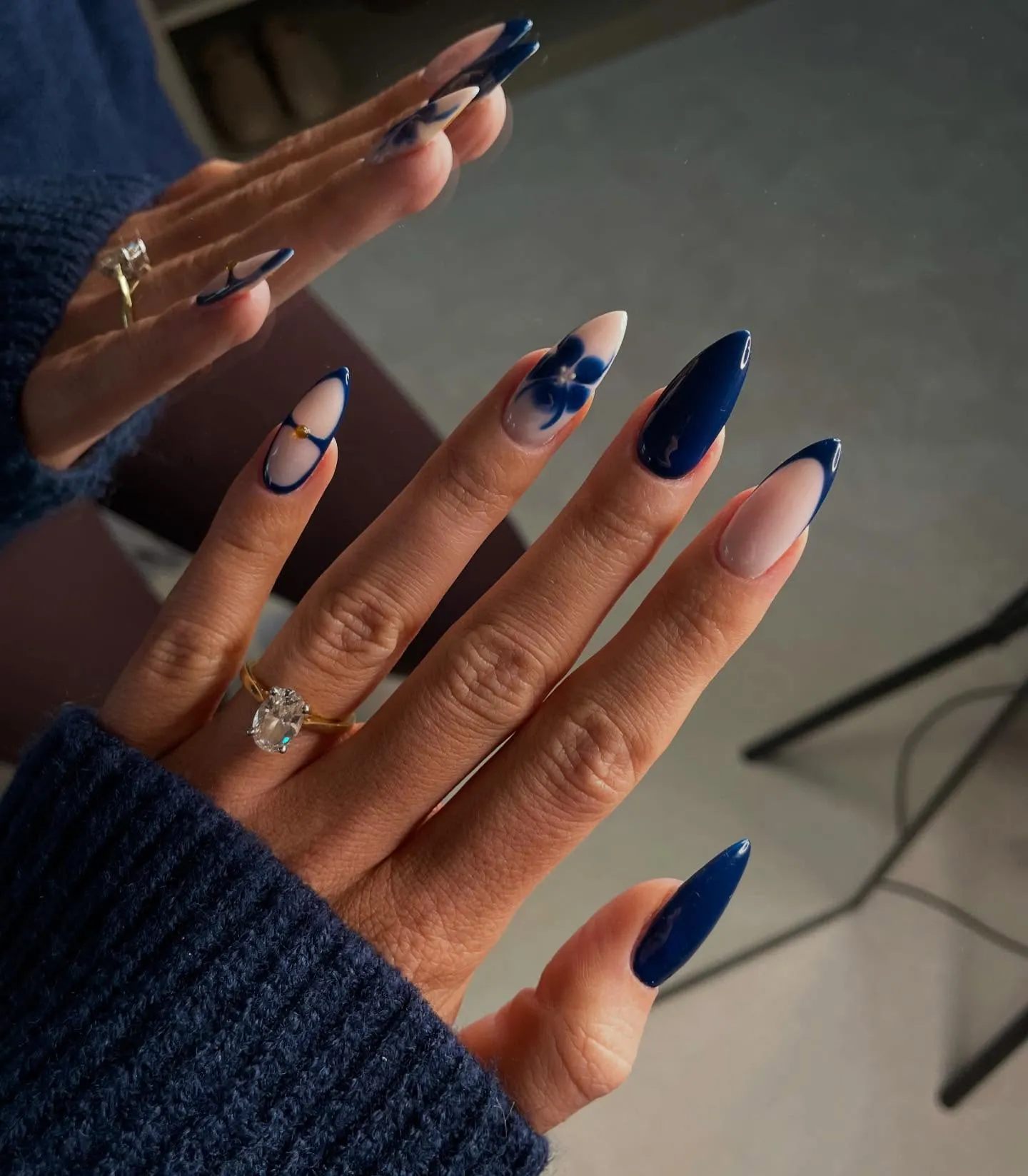 Long almond nails mixing solid navy, nude French tips and a blue flower accent