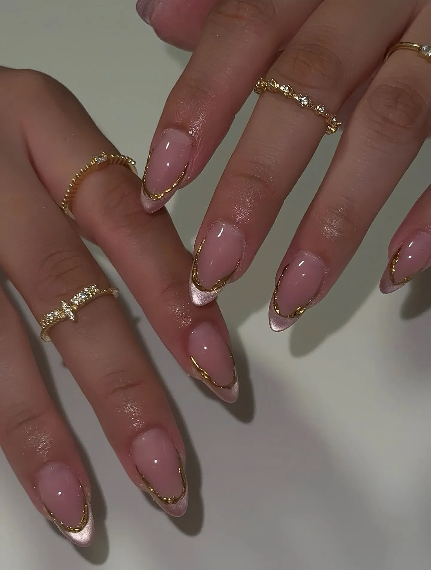 Pink almond nails with pale French tips and fine gold smile lines