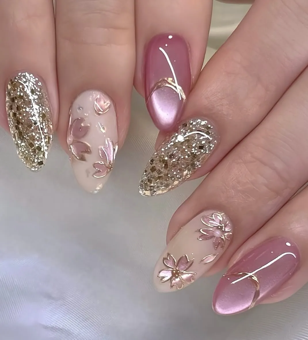 Pink almond nails with full gold glitter accents, flowers and metallic curves