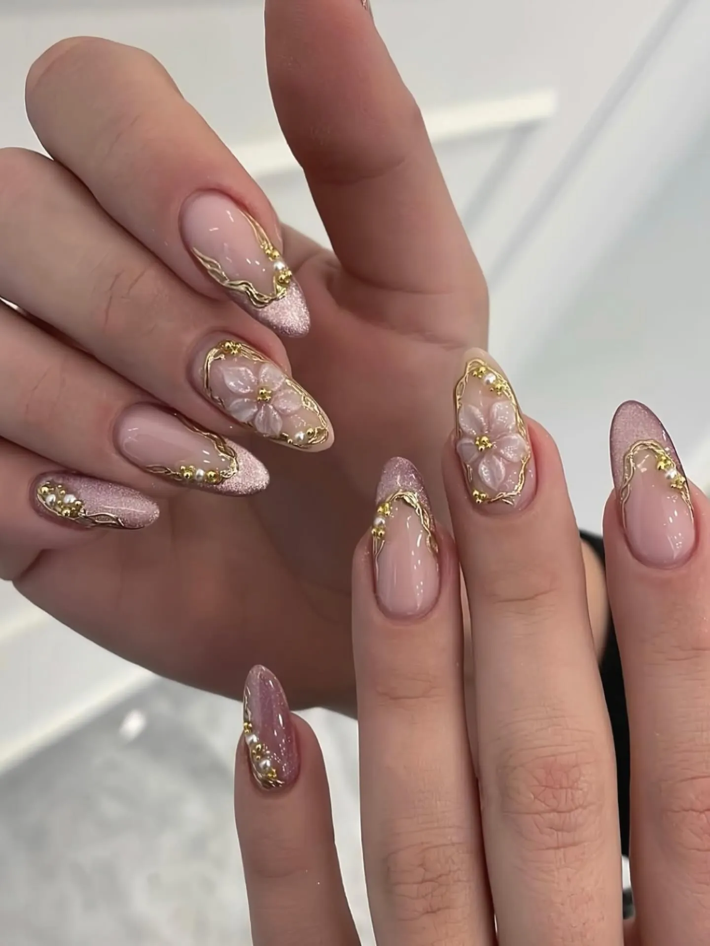Pink almond nails with gold framed accents, pale flowers and textured gold tips
