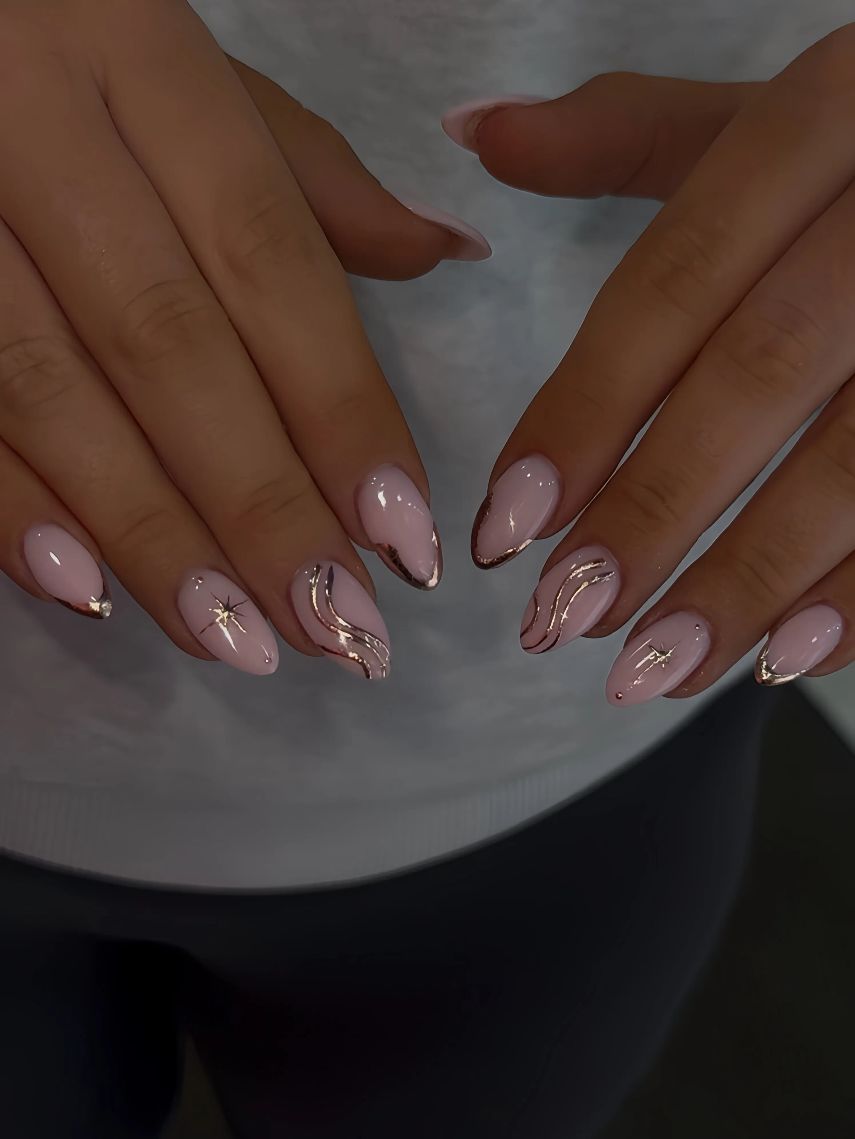 Pink almond nails with flowing pale and gold lines and a small starburst