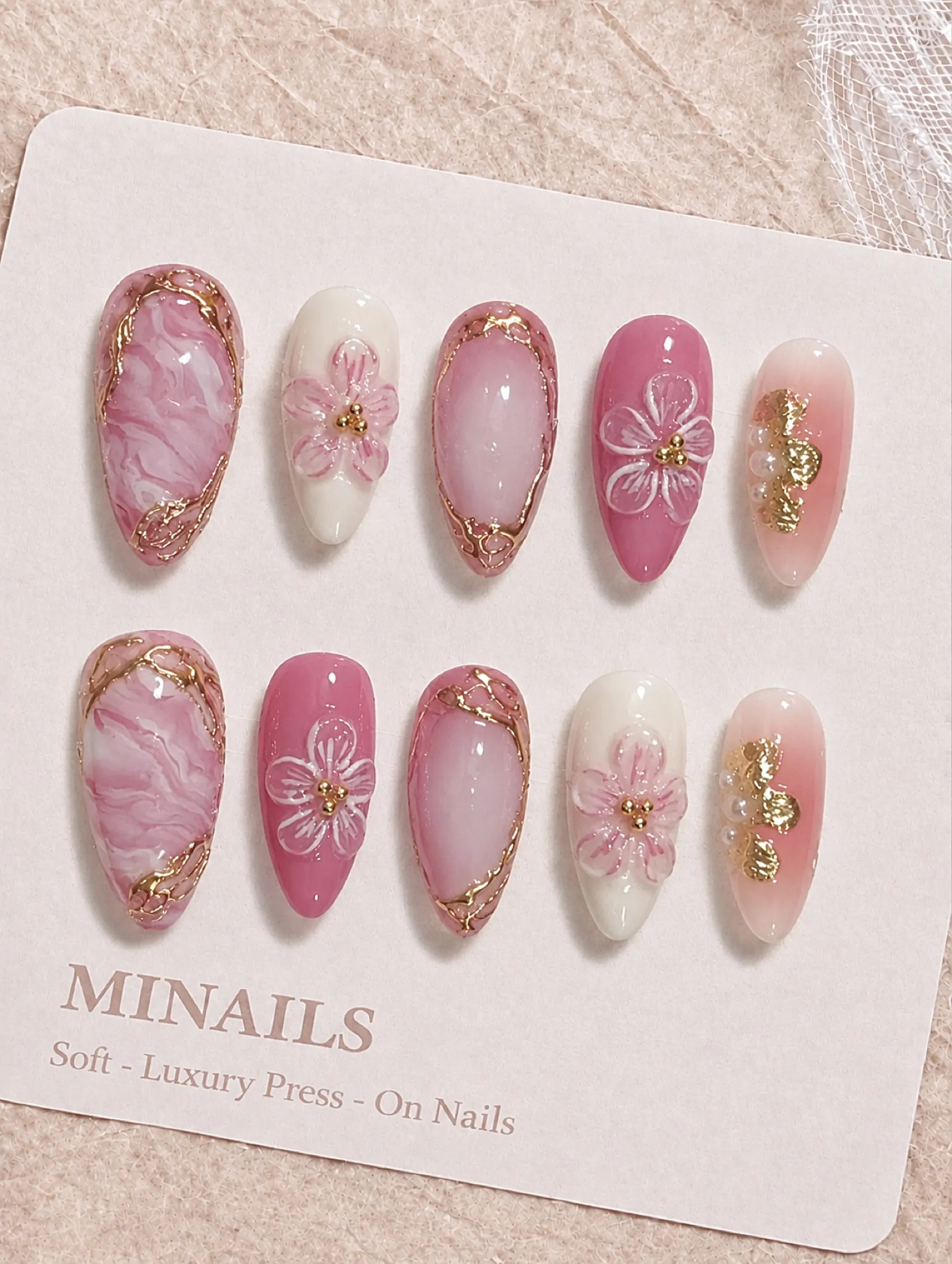 Pink marbled and cream floral nails with gold frames shown on a display card