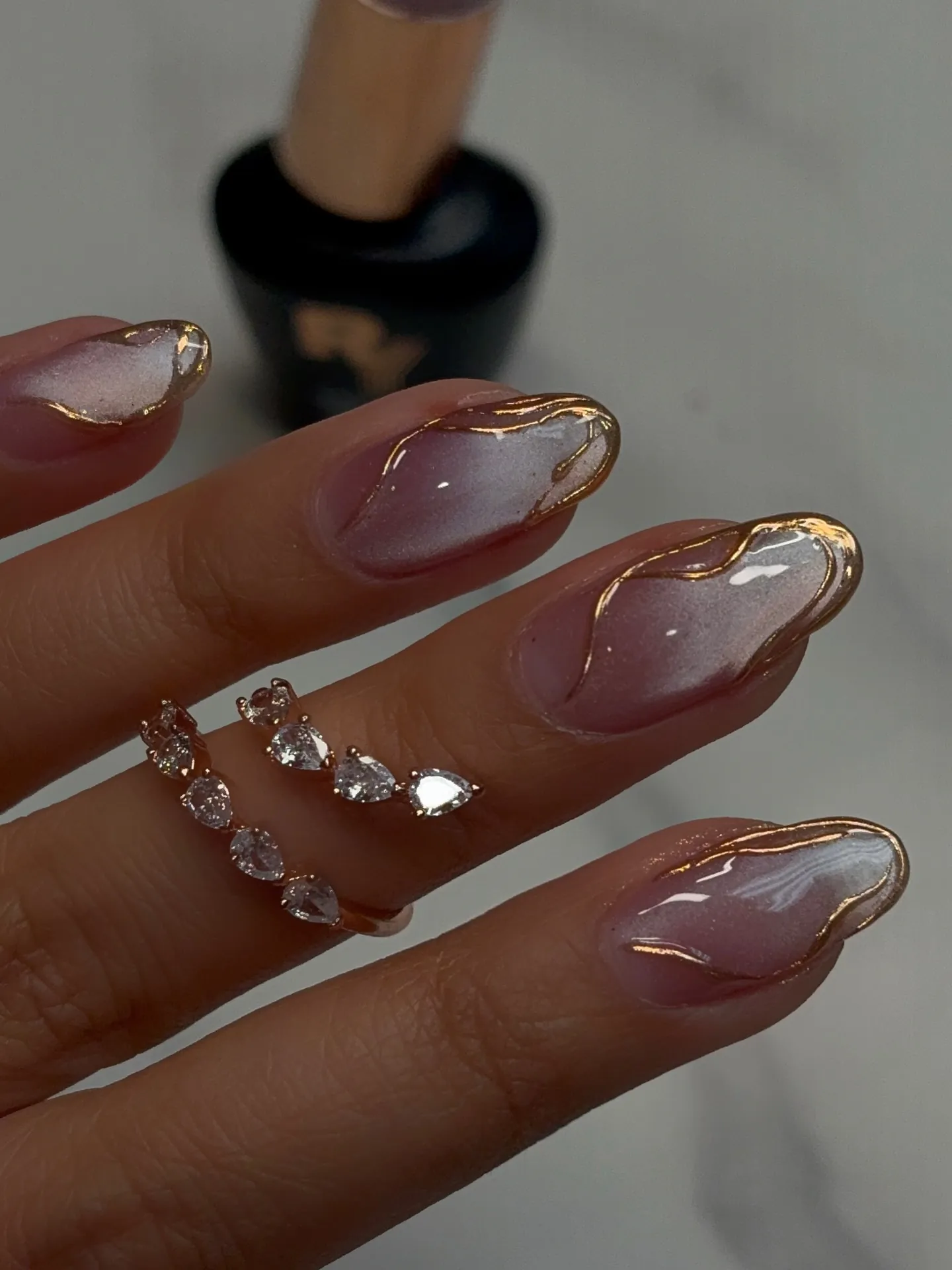 Glossy pink almond nails with irregular gold outlines near the tips
