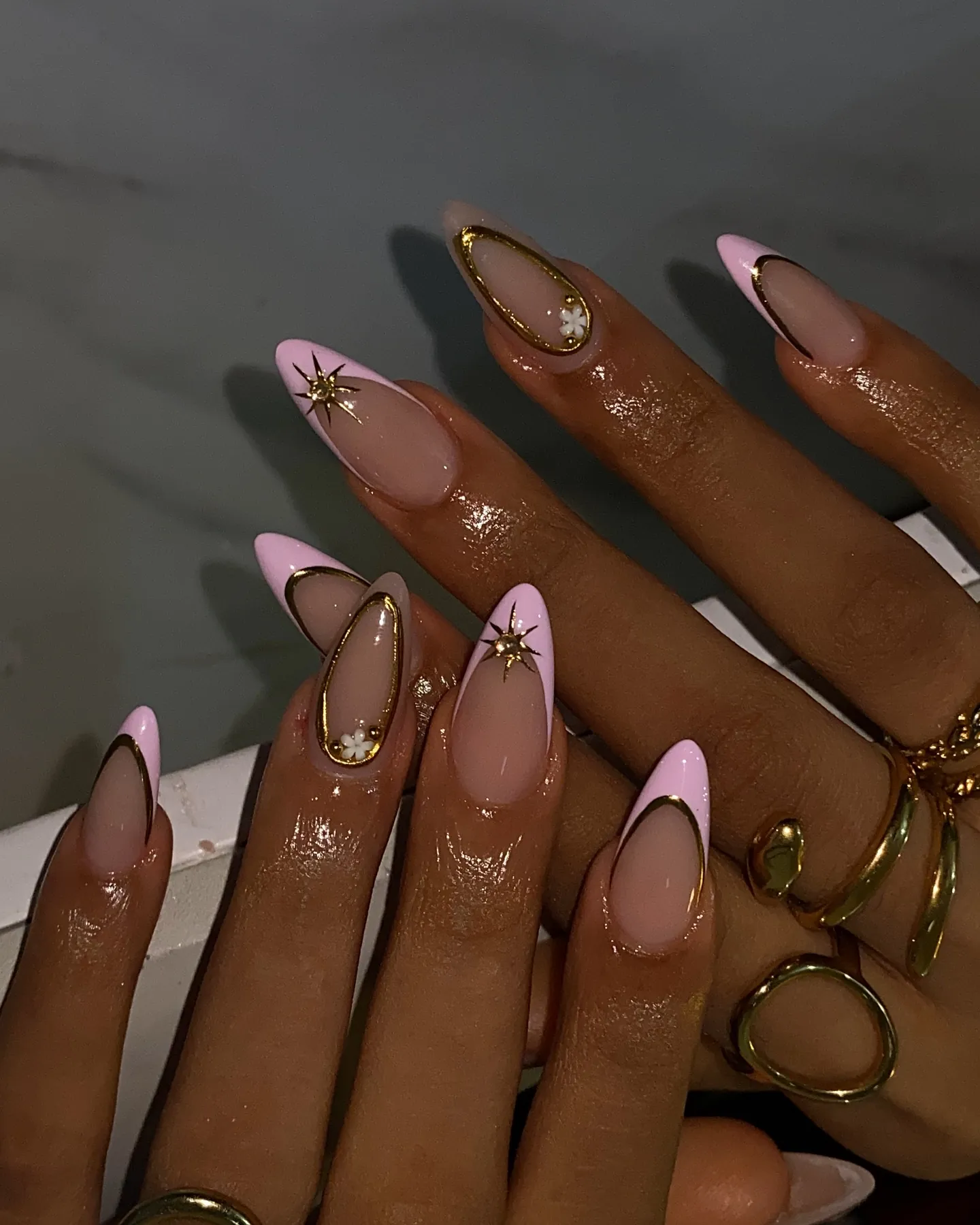 Pink almond French tips outlined in gold with small gold starbursts