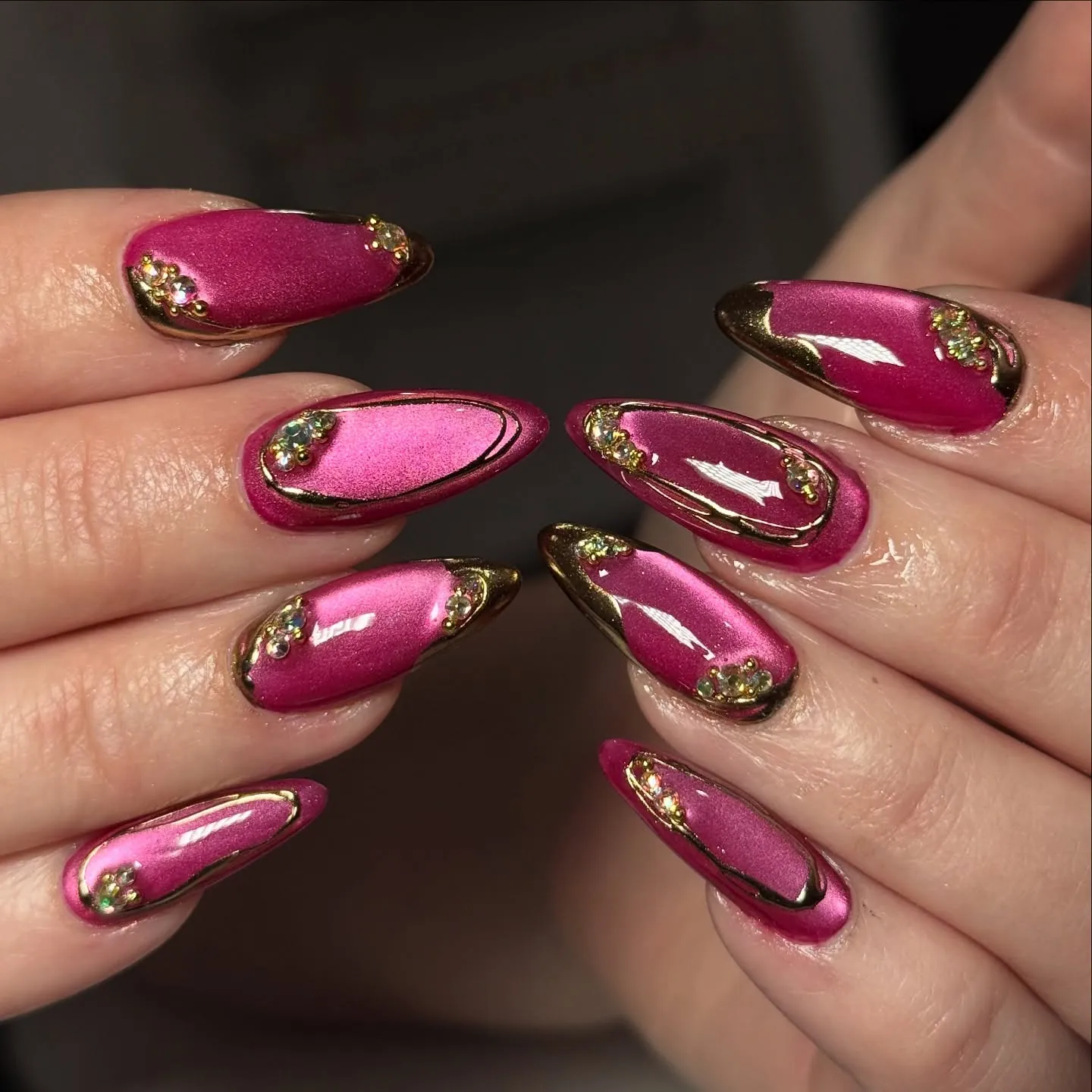 Reflective bright pink almond nails with sculpted gold borders and accents