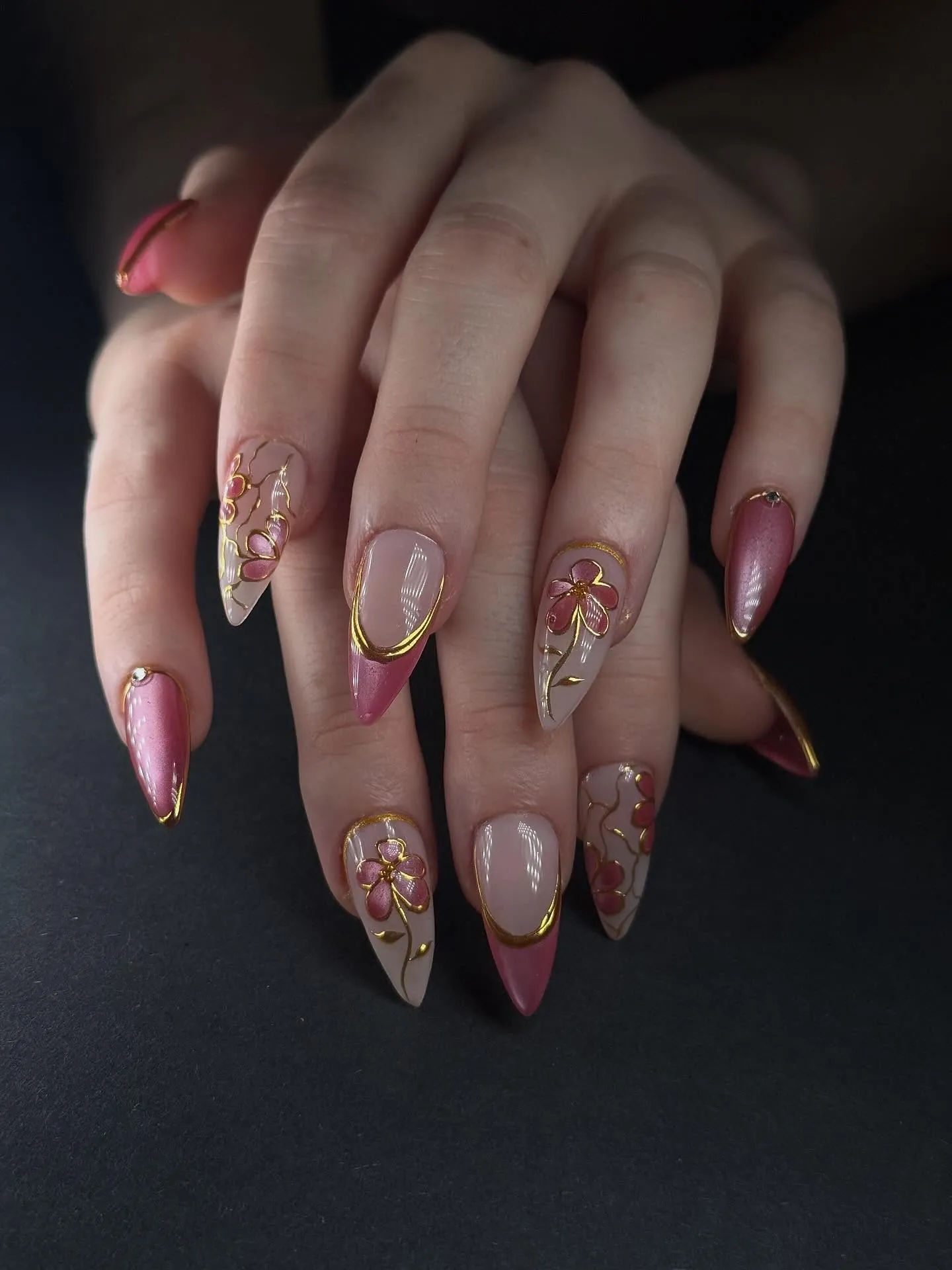Pointed pink nails with gold floral outlines and curved metallic borders