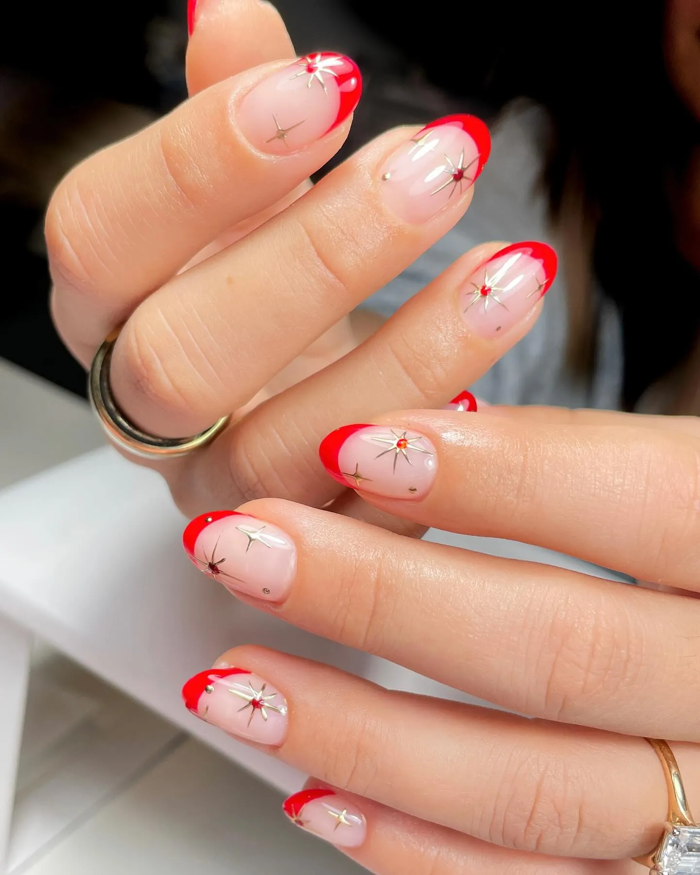 Bright red French tips on pink almond nails with fine metallic starbursts
