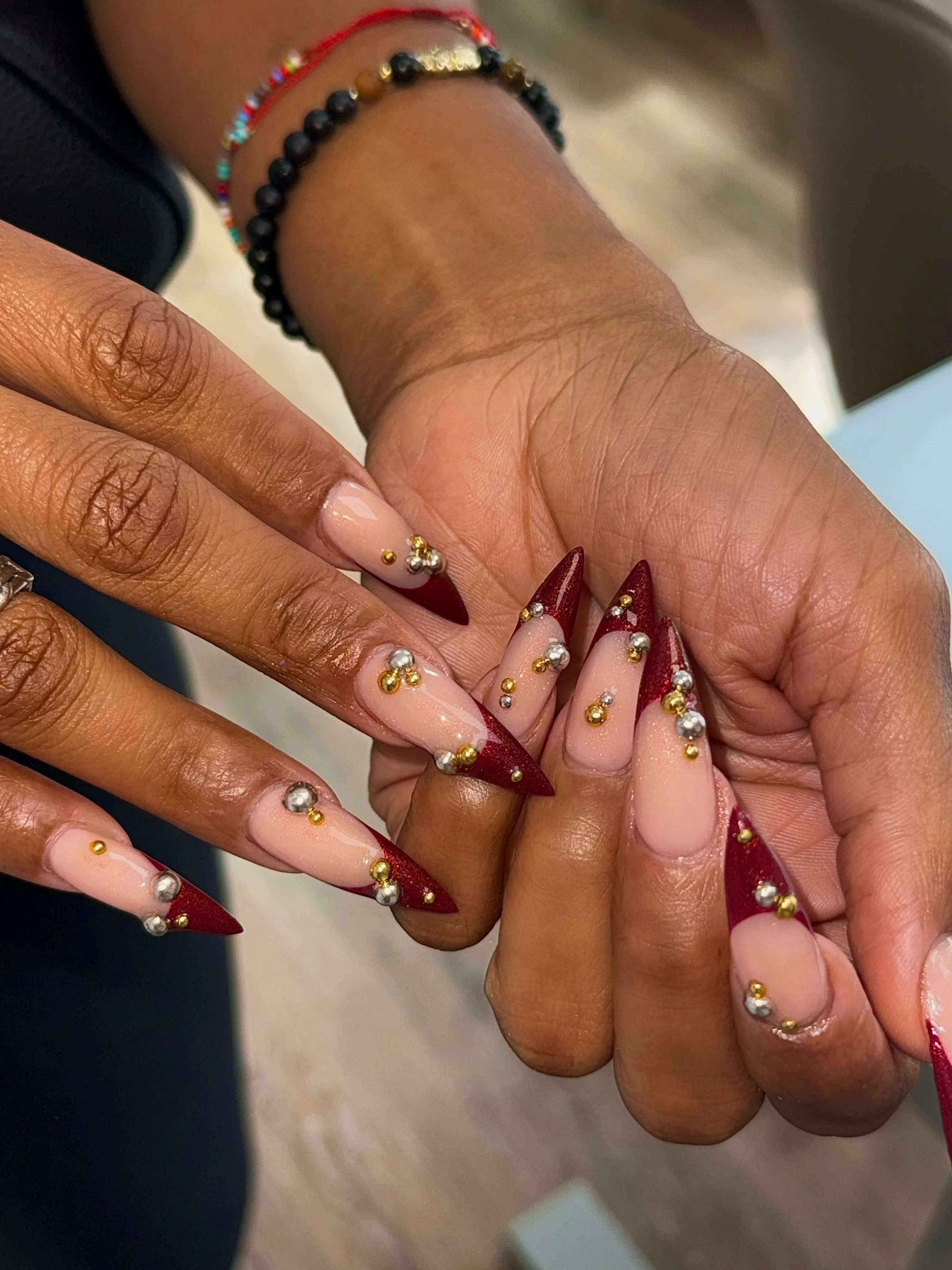 Long pointed burgundy French nails with gold details and clustered bright gems