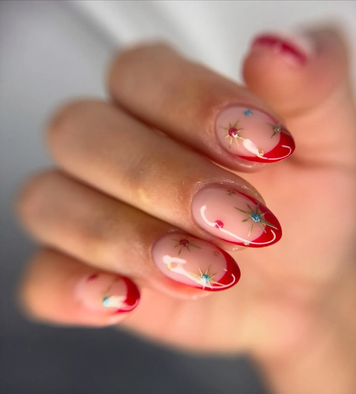 Short red French nails with small multicolored metallic stars on pink bases