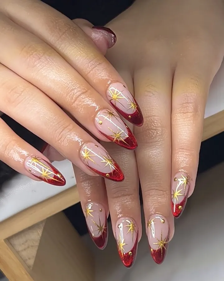 Long almond red French nails with several large gold starbursts