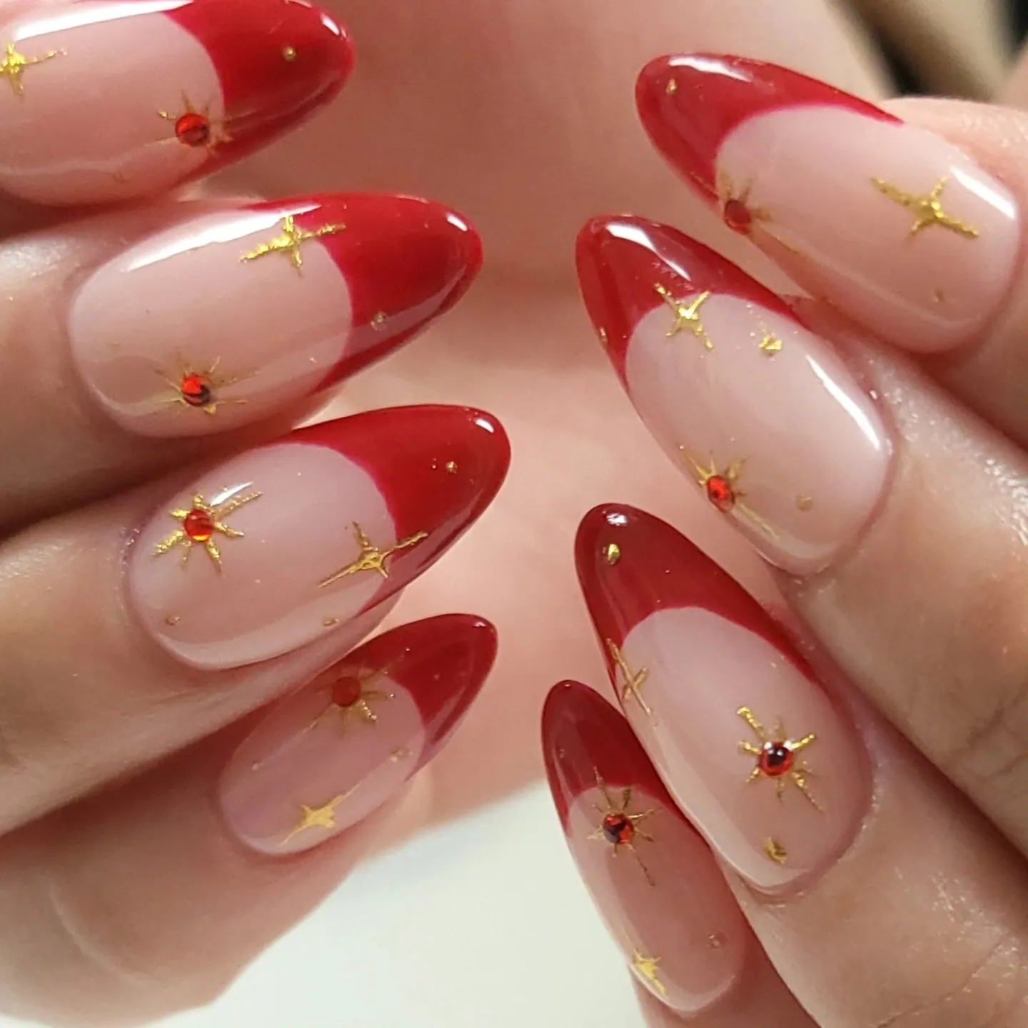 Red almond French nails with gold starbursts and tiny red gem accents