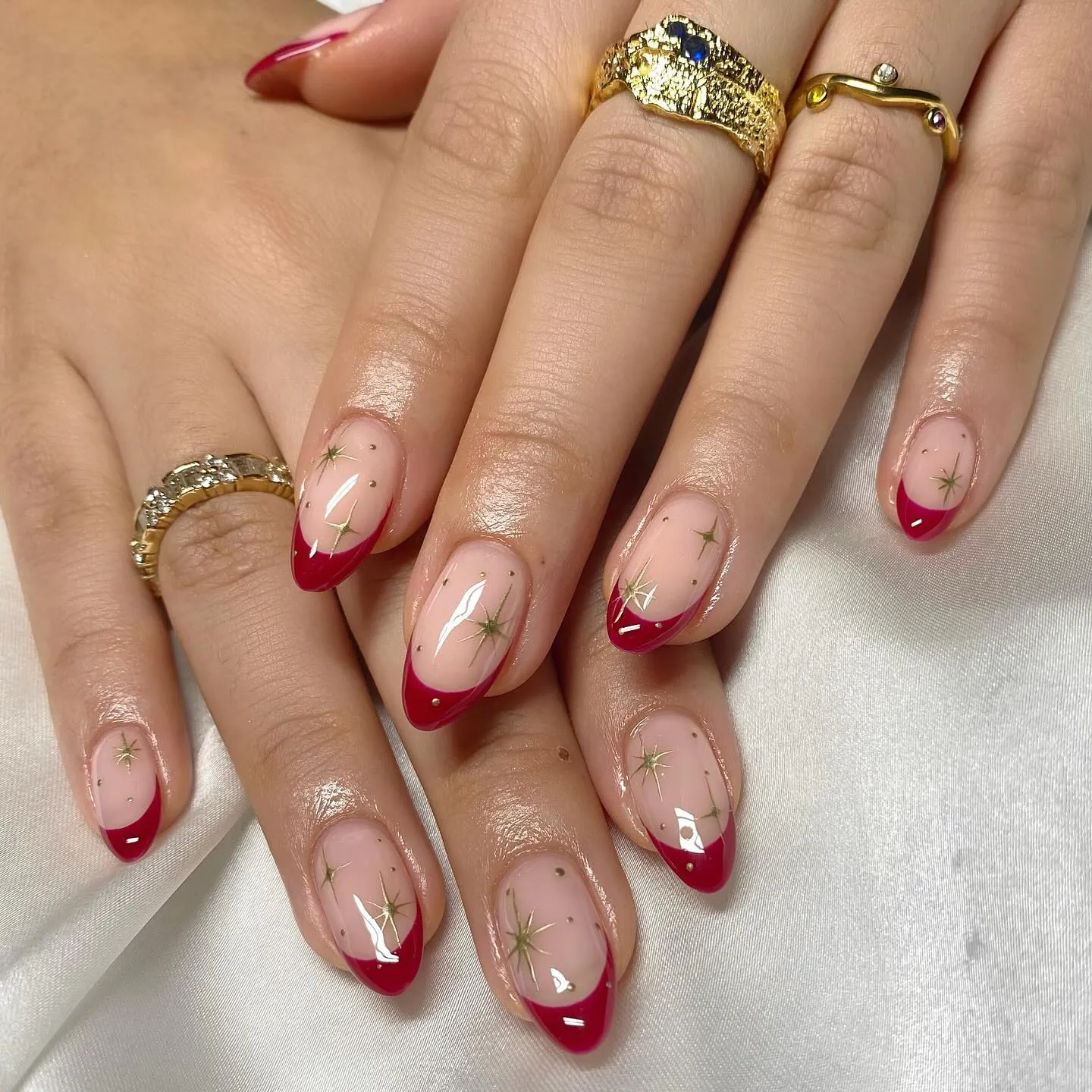 Pink almond nails with red French tips and scattered delicate gold stars