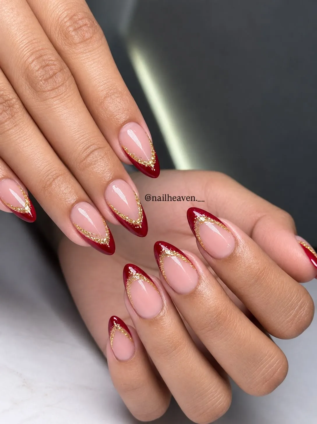 Pink almond nails with red French tips outlined by fine gold glitter