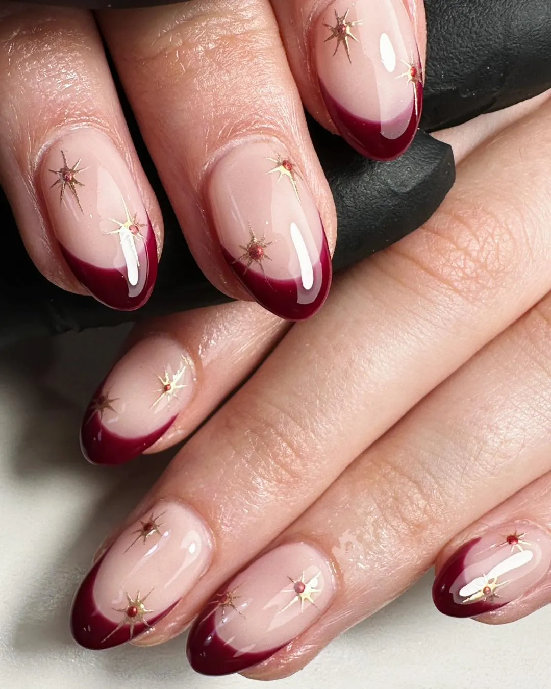 Pink oval nails with burgundy French tips and scattered gold starbursts