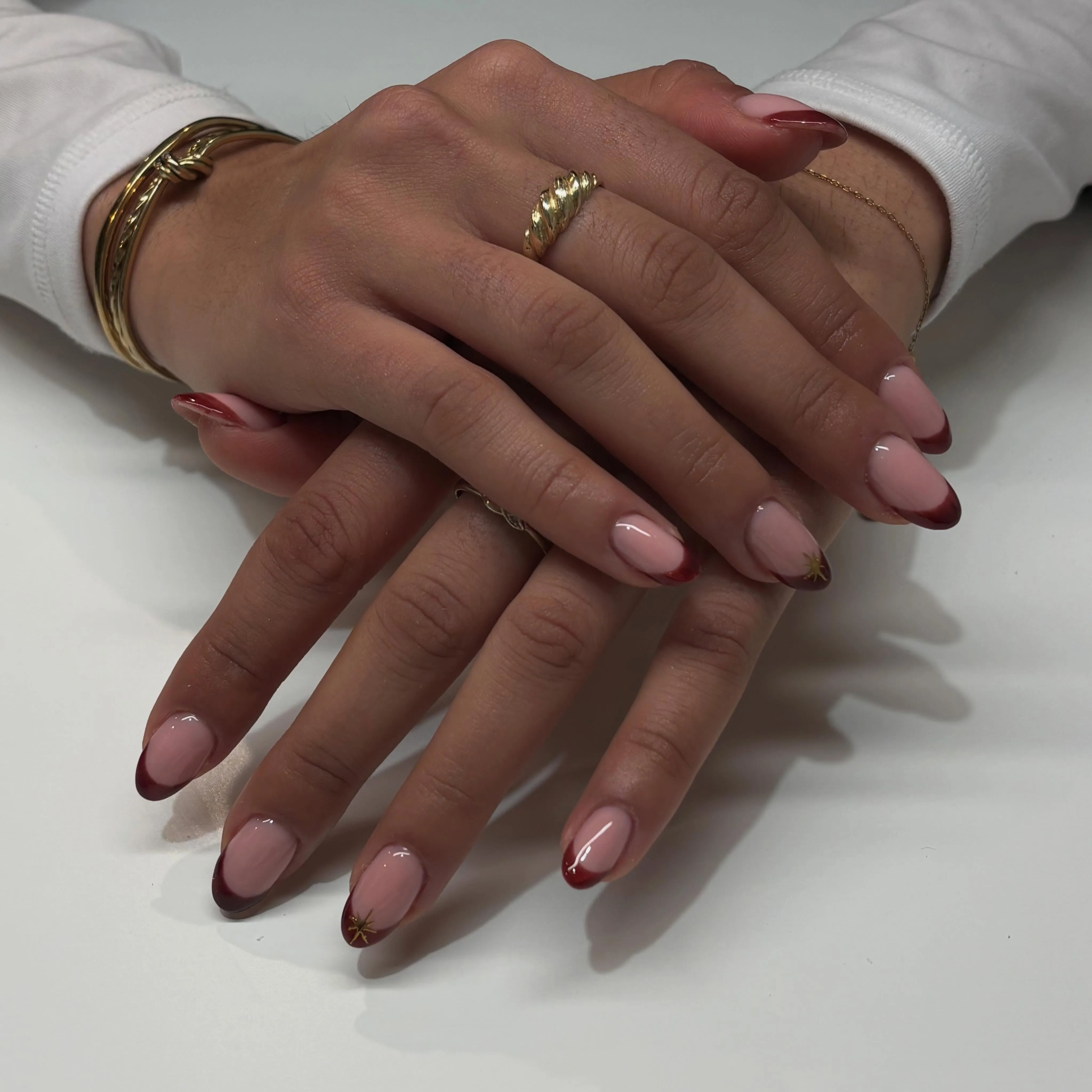 Glossy pink almond nails with dark red French tips and single gold stars