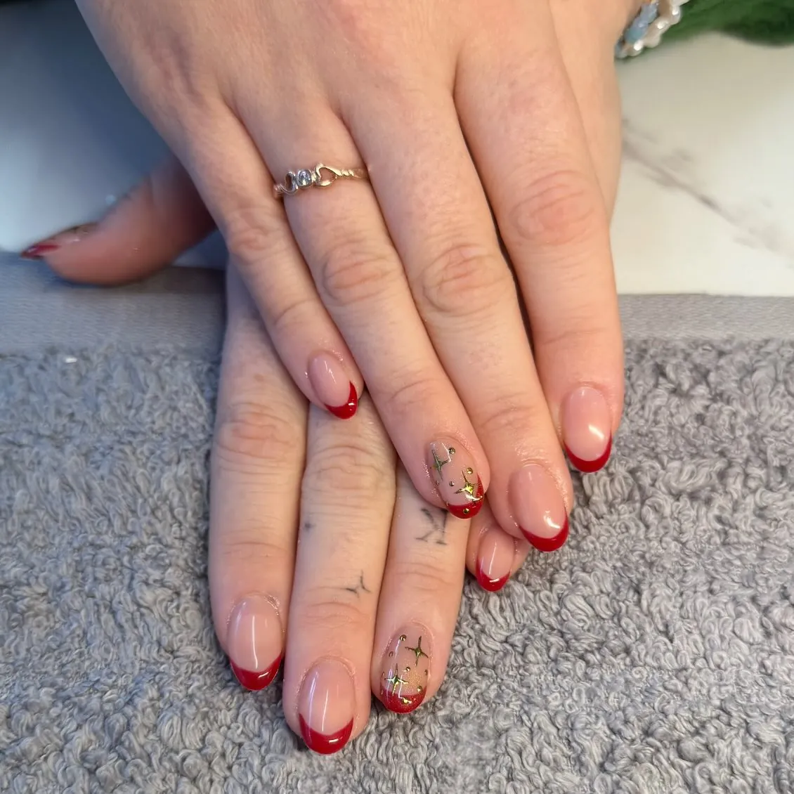 Short rounded pink nails with red French tips and gold stars on accent nails