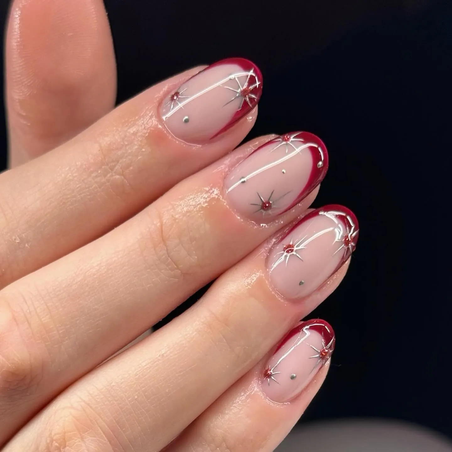 Pink oval nails with dark red tips, silver starbursts and small red gems
