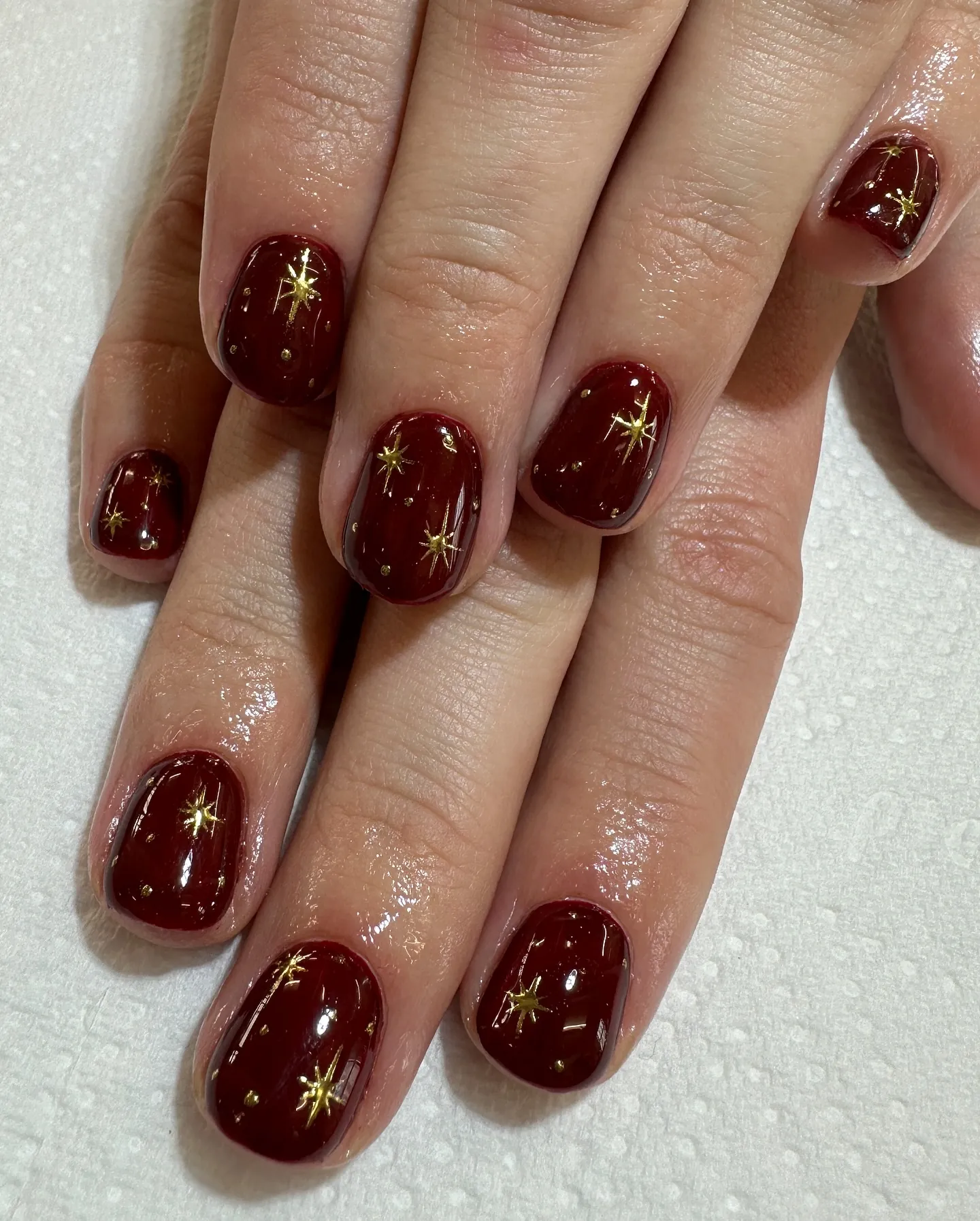 Short rounded square burgundy nails with scattered gold stars and dots