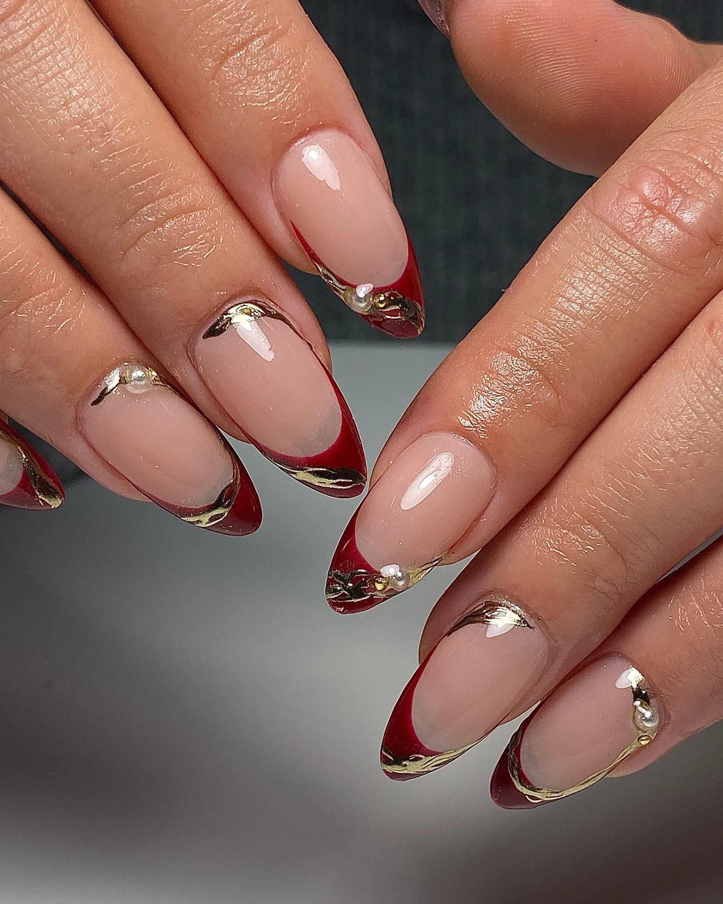 Red almond French tips with gold swirls and small pearl-like accents