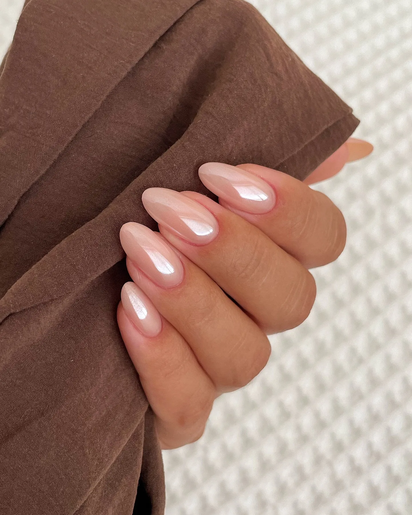 Pale nude pink almond nails with a luminous reflective finish