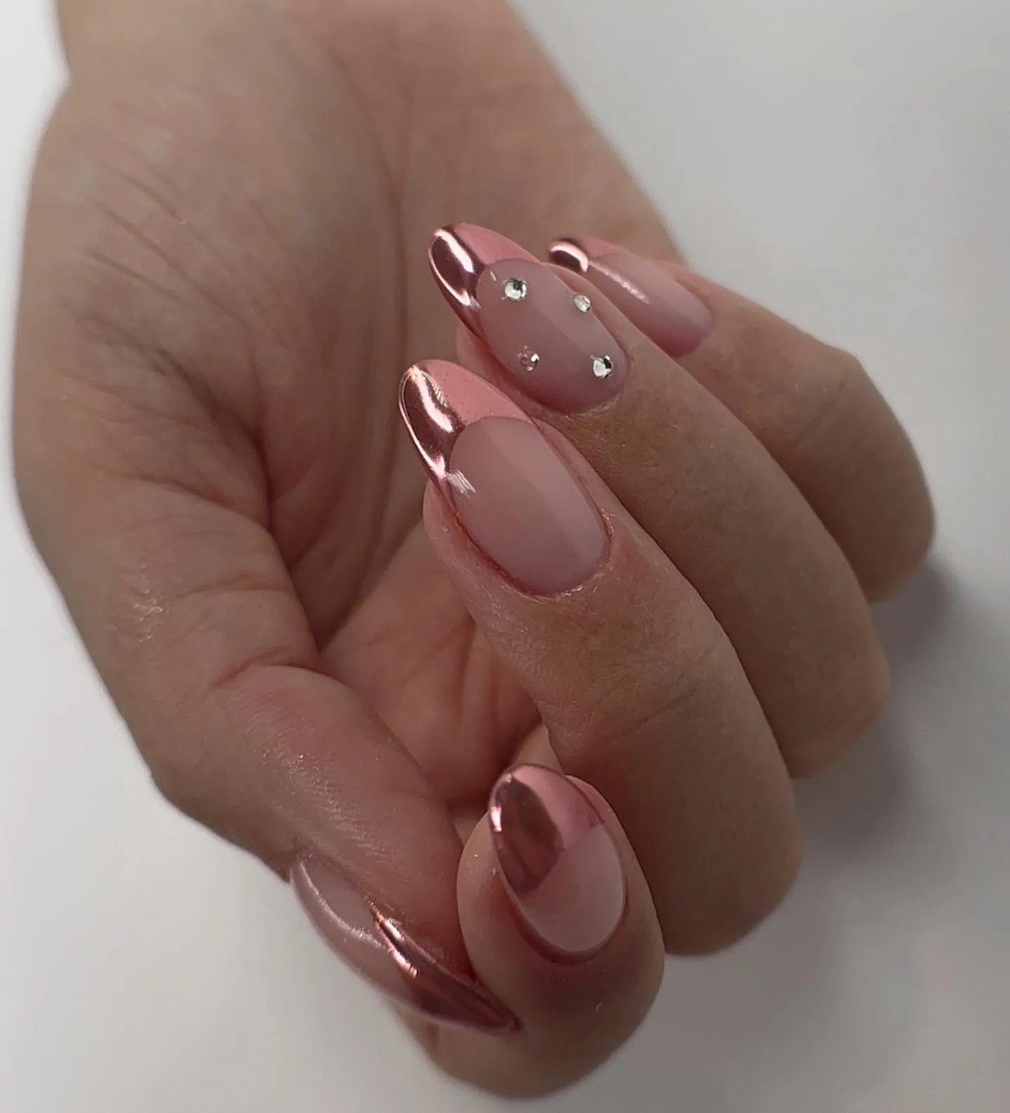 Nude pink almond nails with rose chrome French tips and small crystals