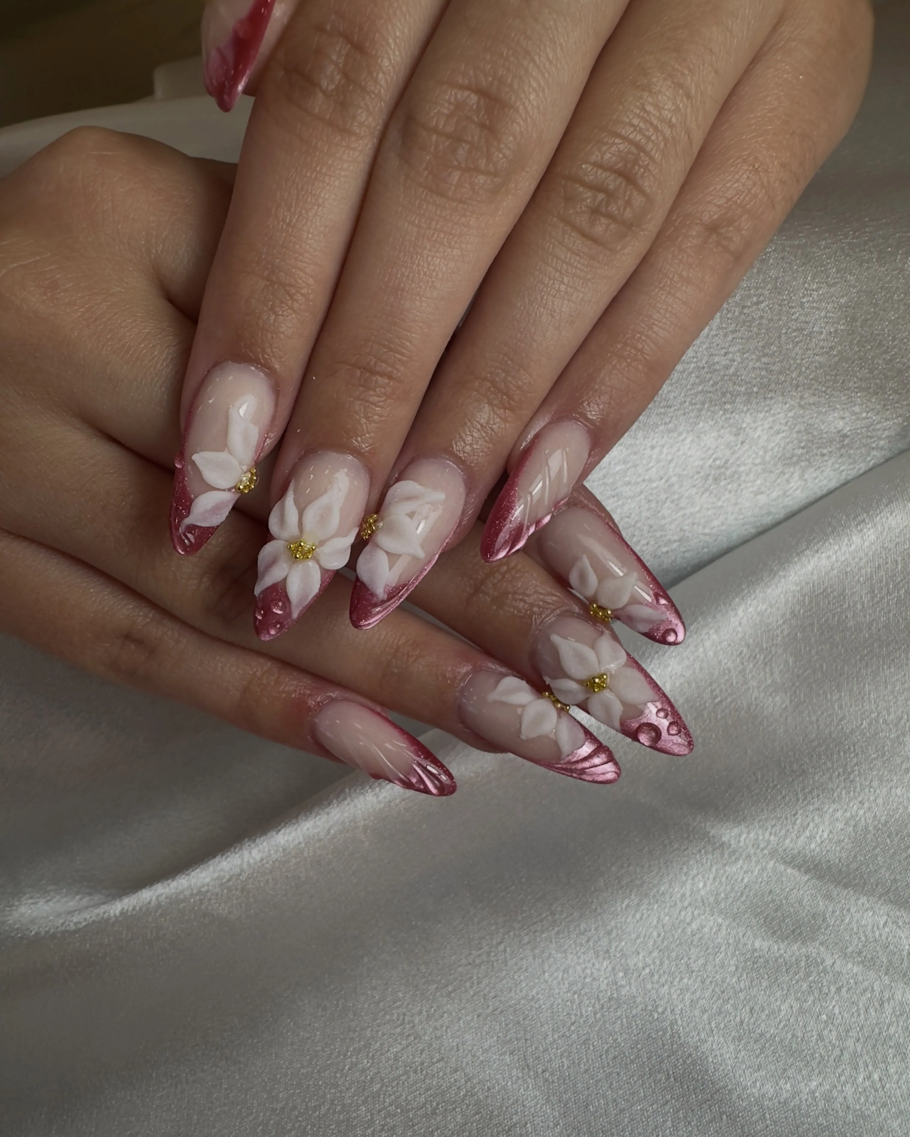 Long pink tipped nails with raised white flowers and gold centers