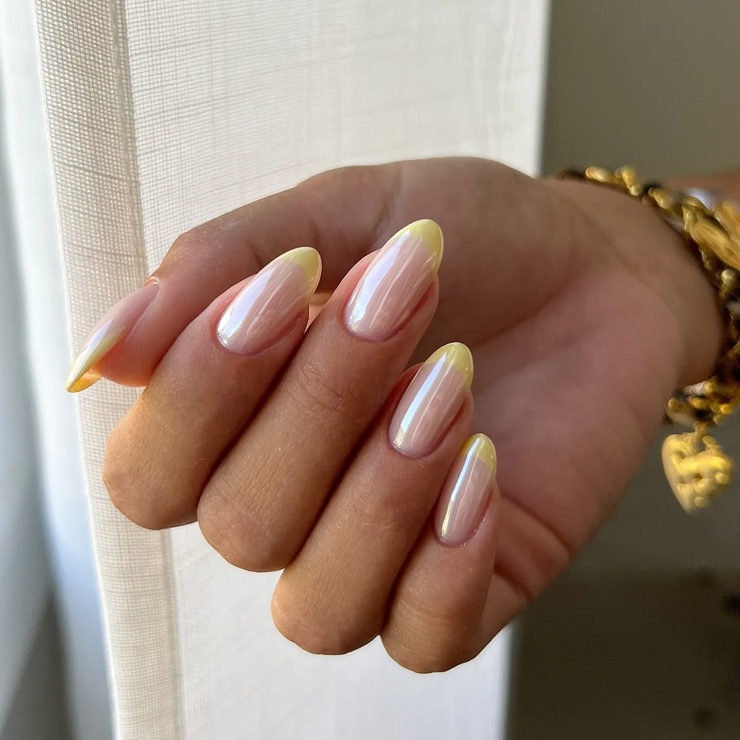 Almond nails with reflective pearly pink bases and soft yellow tips