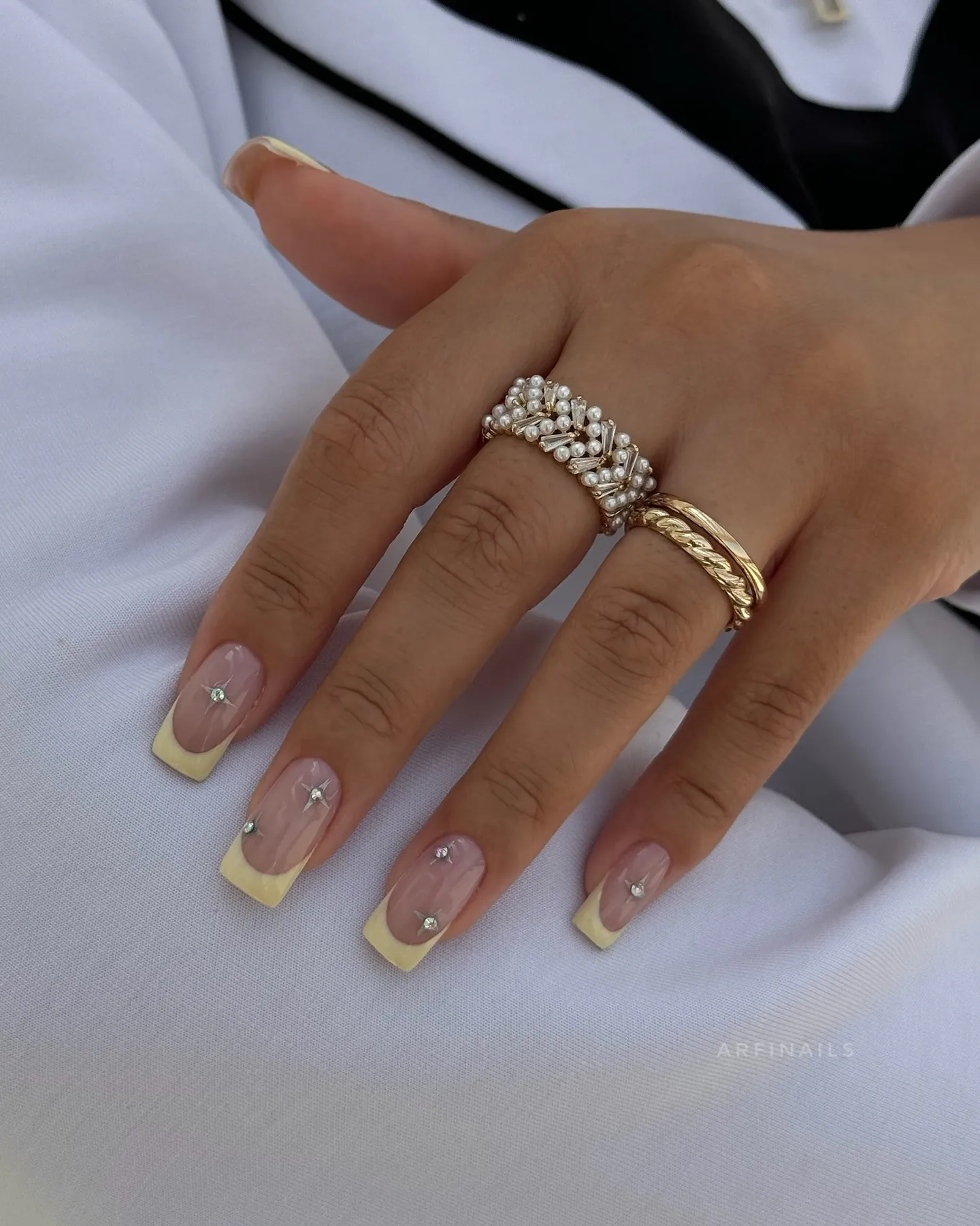 Square yellow French nails with white starbursts and small bright gems