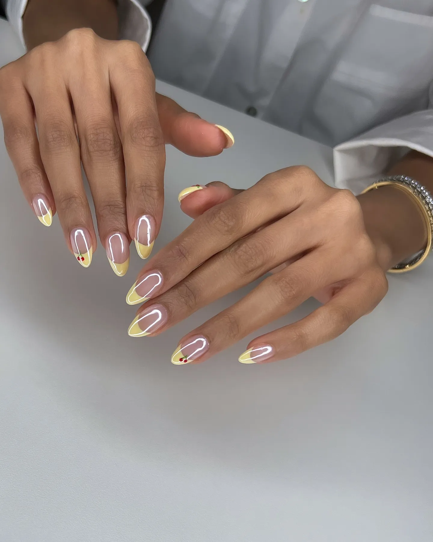 Glossy pink almond nails with pale yellow tips and tiny red cherries