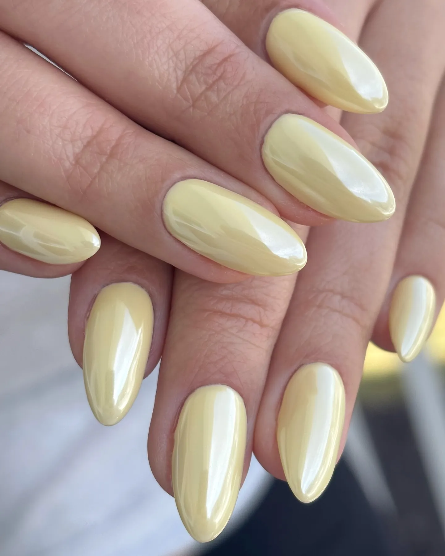 Almond nails fully covered in pale yellow with a reflective pearly sheen