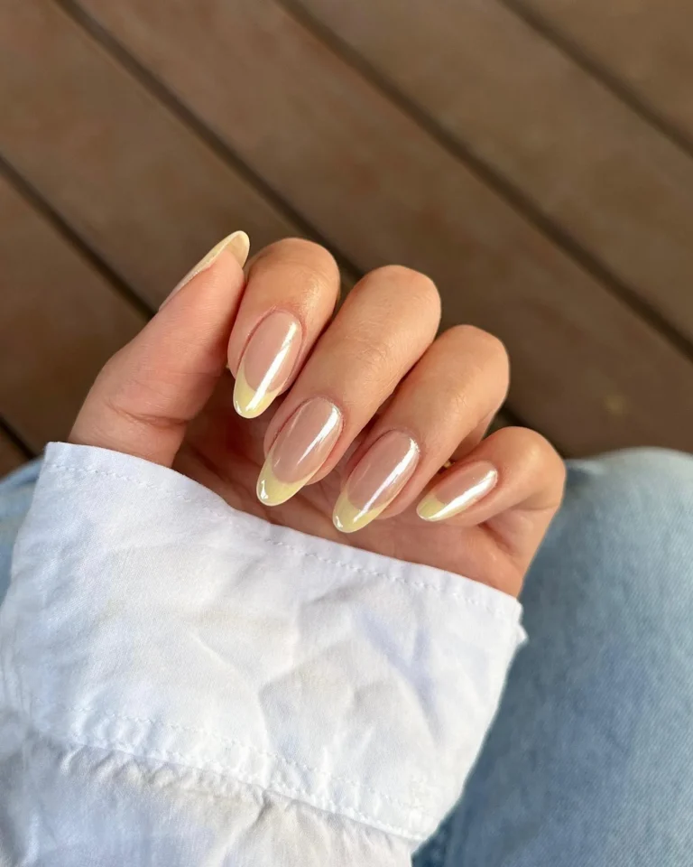 Glossy nude almond nails with pale yellow chrome French tips and a pearlescent sheen