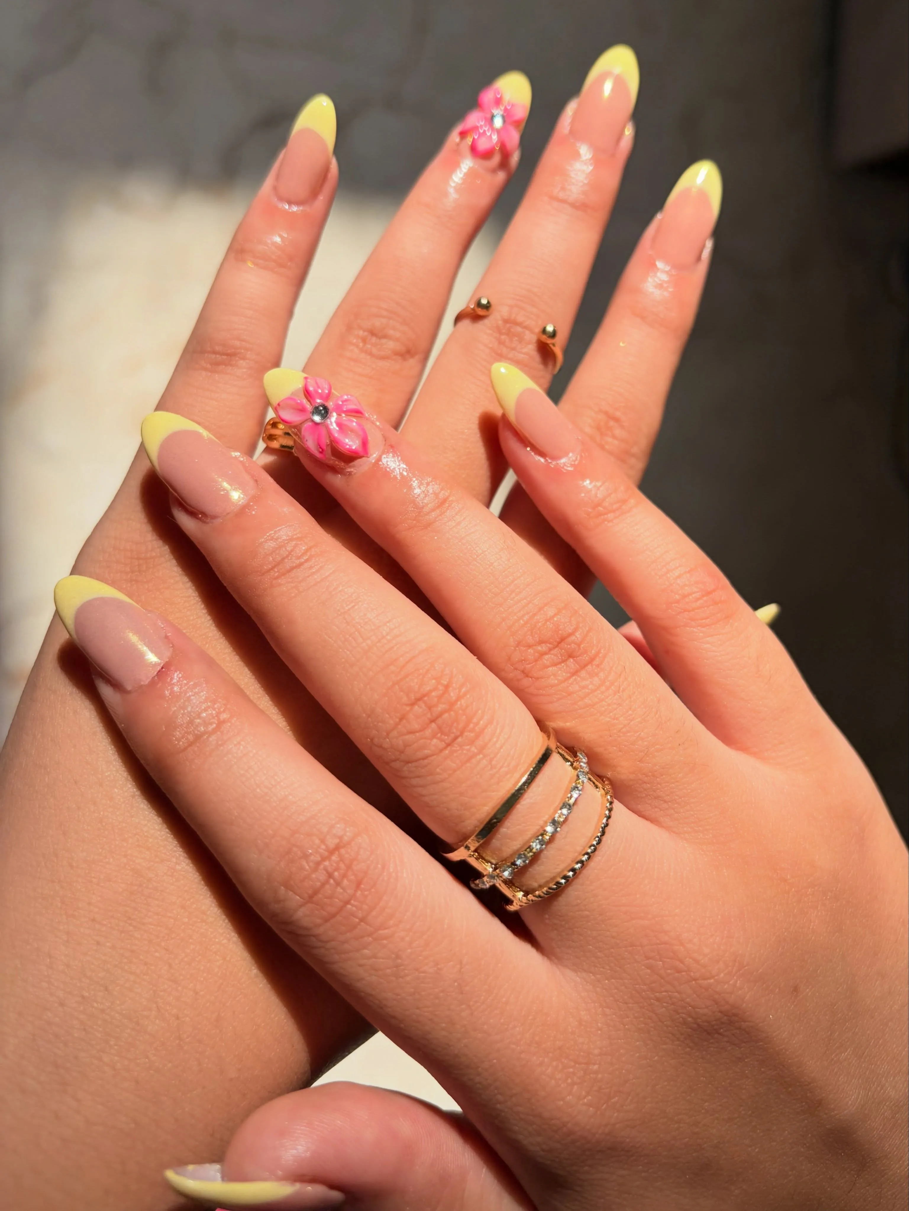 Long almond nails with pale yellow tips and raised pink flower accents