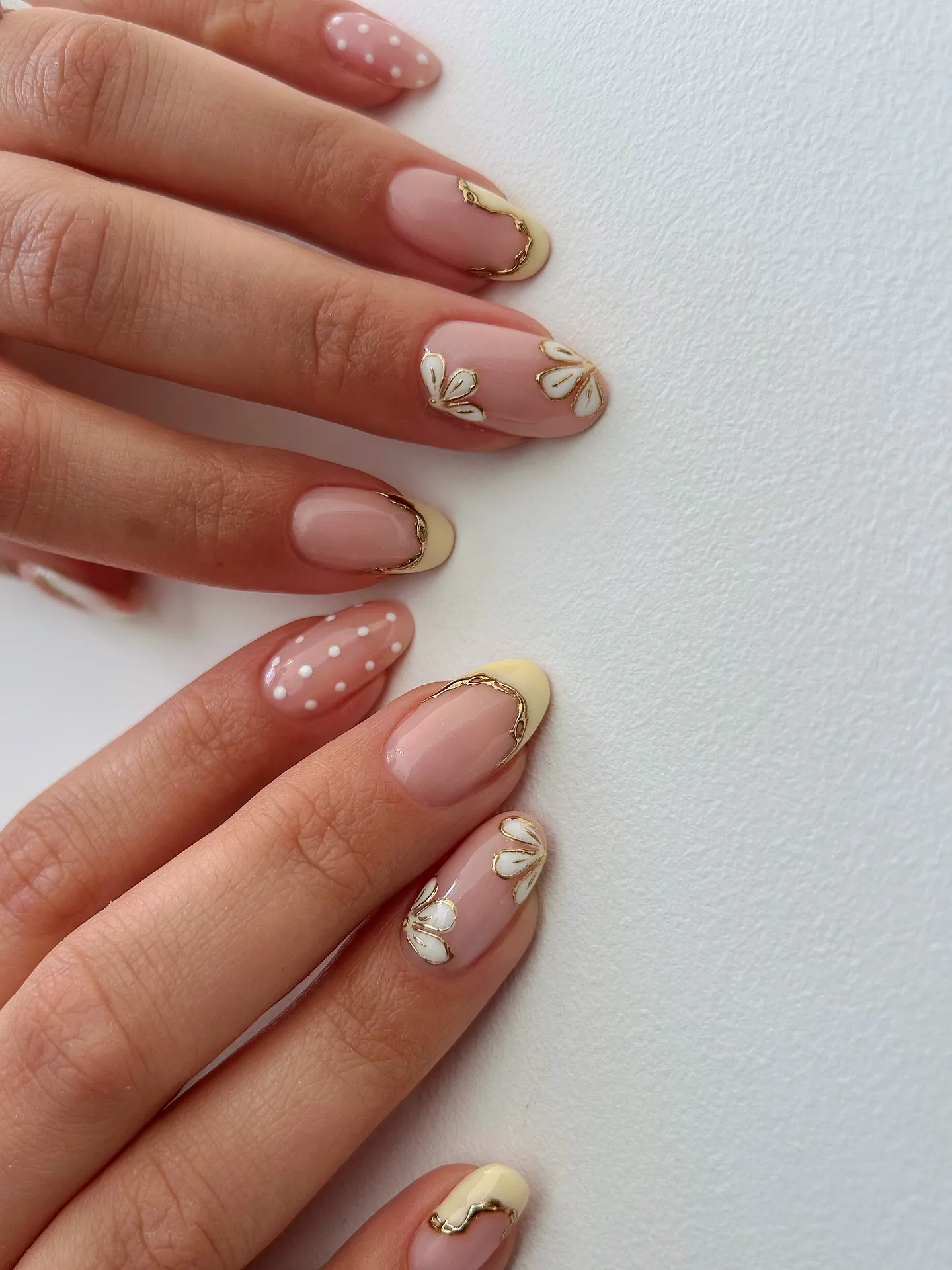 Pale yellow French nails with gold borders, white petals and dotted pink accents