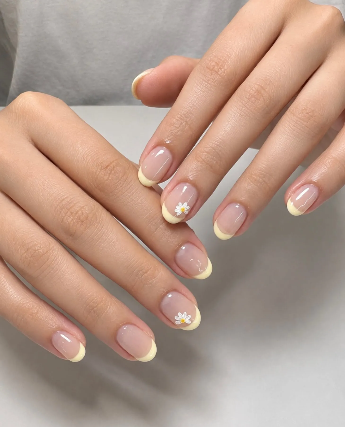 Short rounded pink nails with pale yellow French tips and white daisies