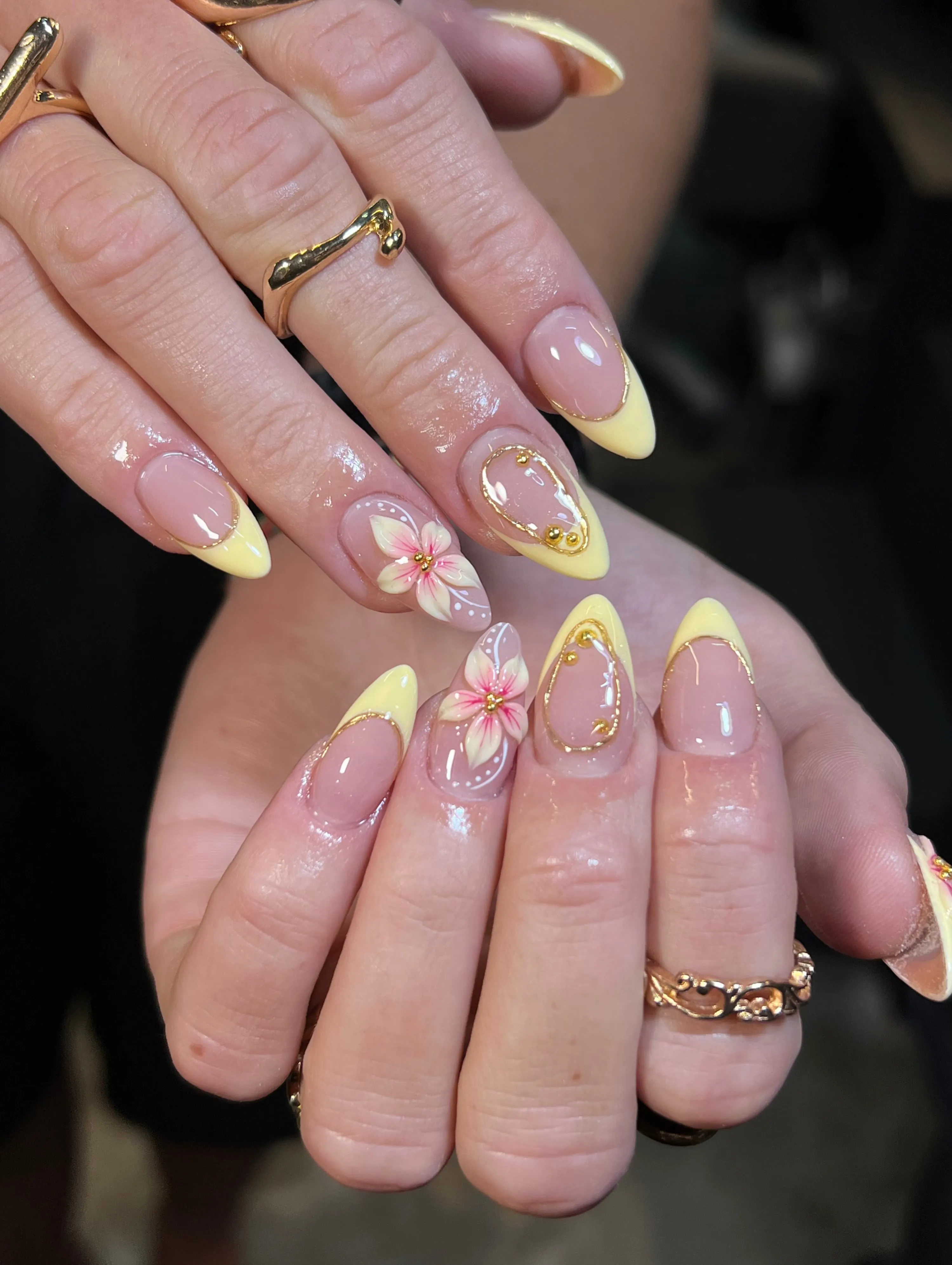 Pale yellow almond French tips with pink-centered flowers and gold outlines